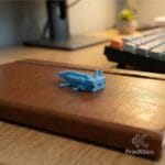 Figura de axolote azul cielo sobre una libreta de cuero marrón en un entorno de oficina home office.