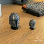 Dos figuras de cascos del Mandaloriano de Pracktico sobre un escritorio de madera con un teclado mecánico borroso al fondo, estilo setup gamer.