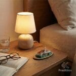 Figura decorativa de Monserrate sobre una mesa de noche de madera iluminada por una lámpara cálida junto a gafas y un libro.