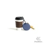 Detalle de llavero forma de café con etiqueta azul redonda y llaves doradas.