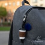 Llavero de café Pracktico colgado en el cierre de una mochila gris estilo urbano.